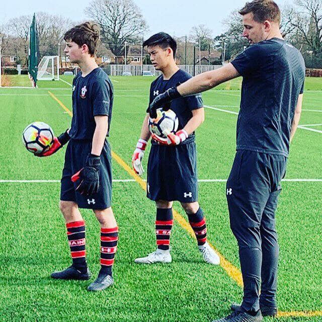 Two Soccer Field Academy goalkeepers in gloves listening to their goalkeeper coach during a training session